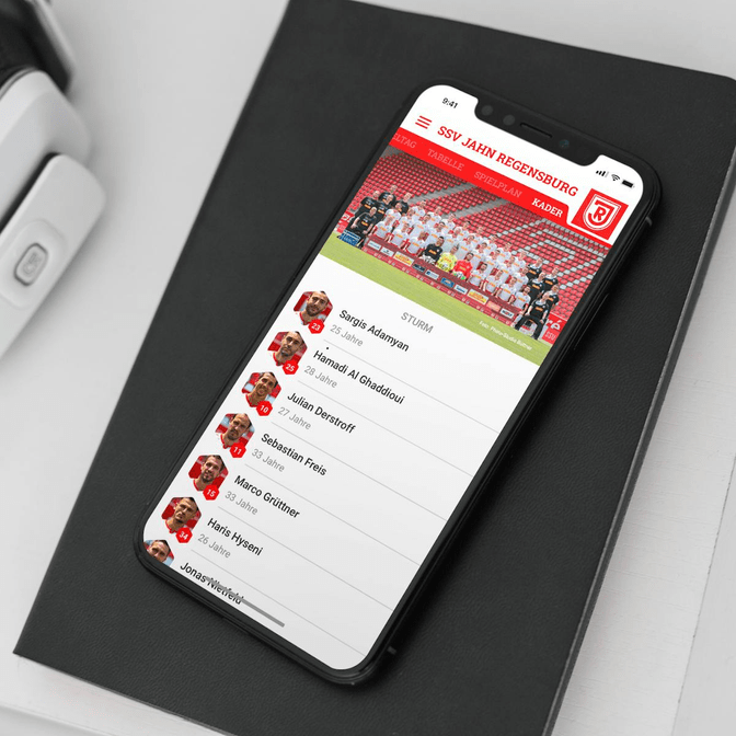 Ein Bild eines iPhones auf einem Schreibtisch, auf dem die App des SSV Jahn Regensburg geöffnet ist.