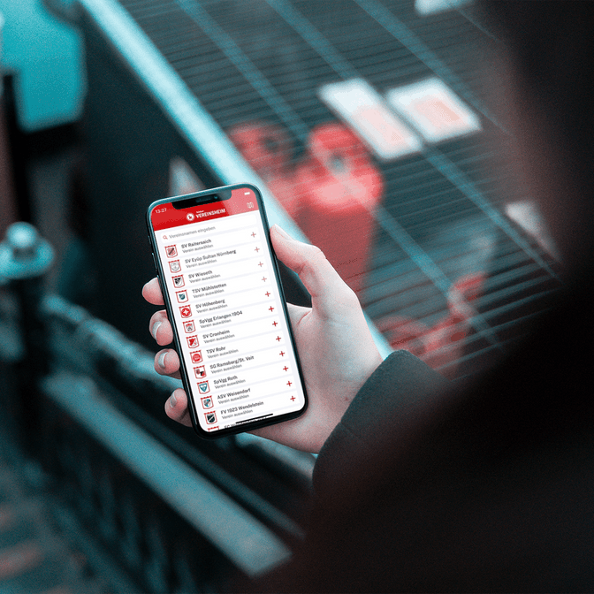 Eine Aufnahme einer Person über die Schulter, die ein iPhone mit der Vereinsheim-App von kicker hält.