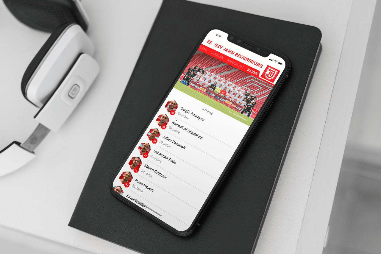 Ein Bild eines iPhones auf einem Schreibtisch, auf dem die App des SSV Jahn Regensburg geöffnet ist.