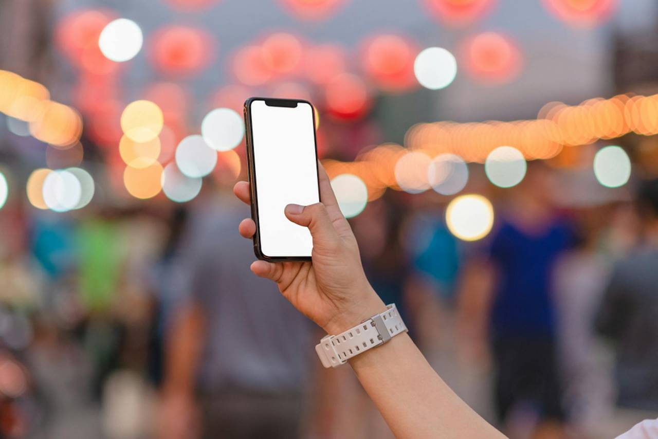 An image of an iPhone with a white screen being held in front of a blurred out background.