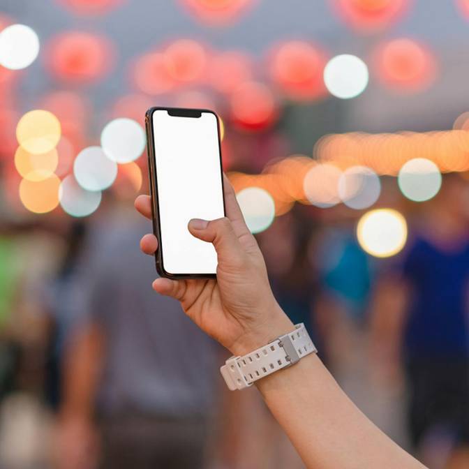 An image of an iPhone with a white screen being held in front of a blurred out background.